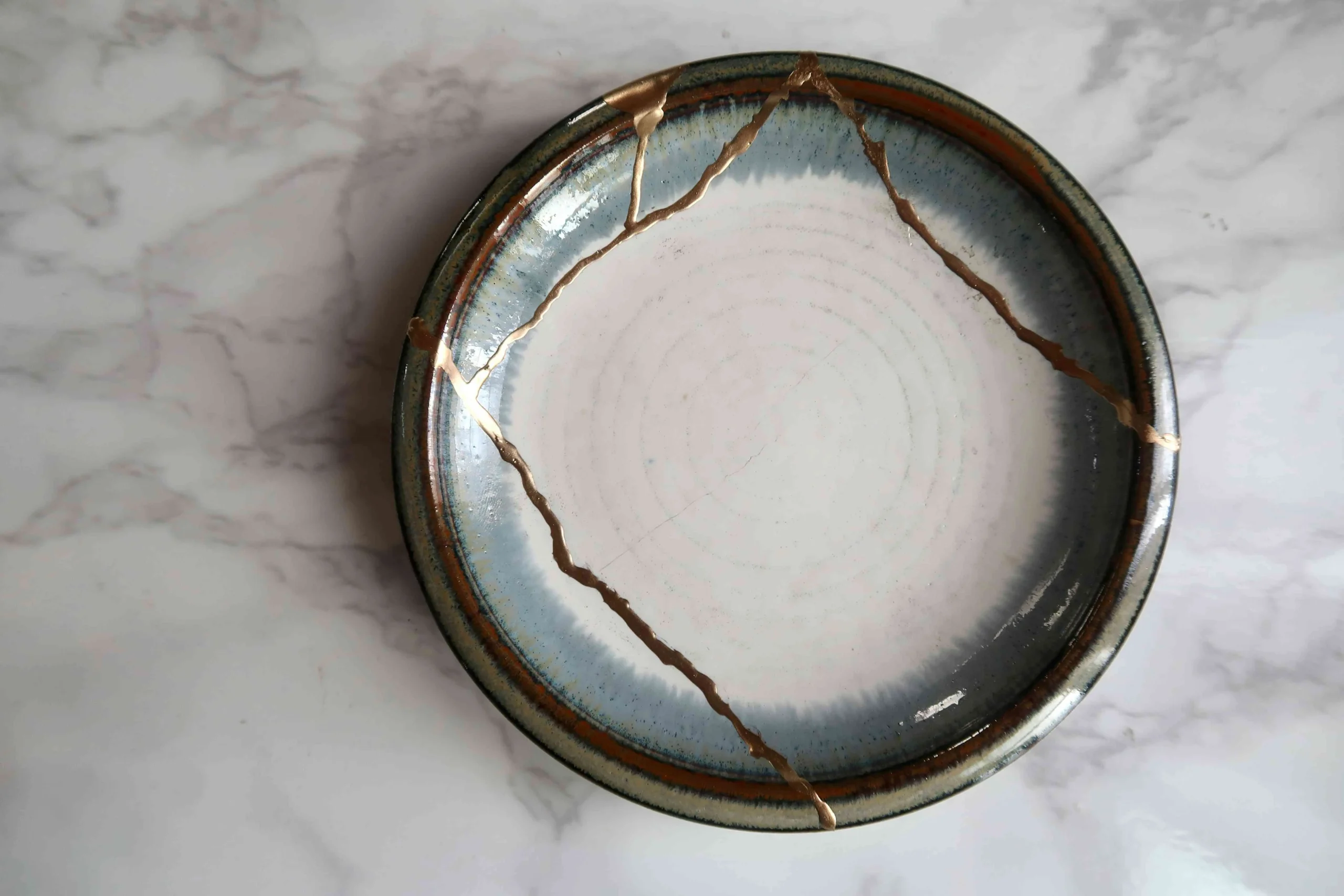 A close-up of a ceramic plate with cracks repaired with gold paint, showcasing the beauty of kintsugi.